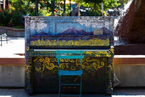 A piano painted in colors of blue and yellow sits in Old Town Square