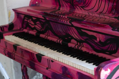A piano painted in colors of pink and purple sits in a parking garage