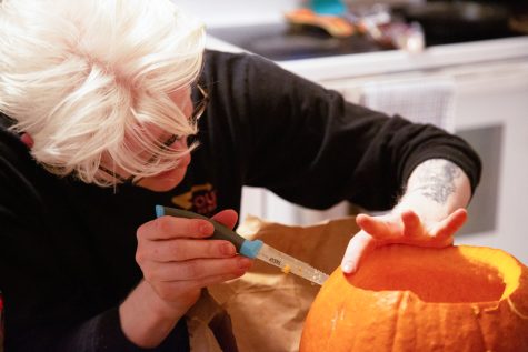Miles Buchan, Collegian cannabis reporter, holds a pumpkin while cutting a precise hole into it for a mouthpiece