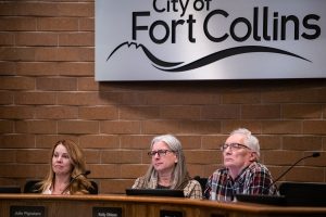 Three people sit behind a wooden stand with a sign reading City of Fort Collins behind them.