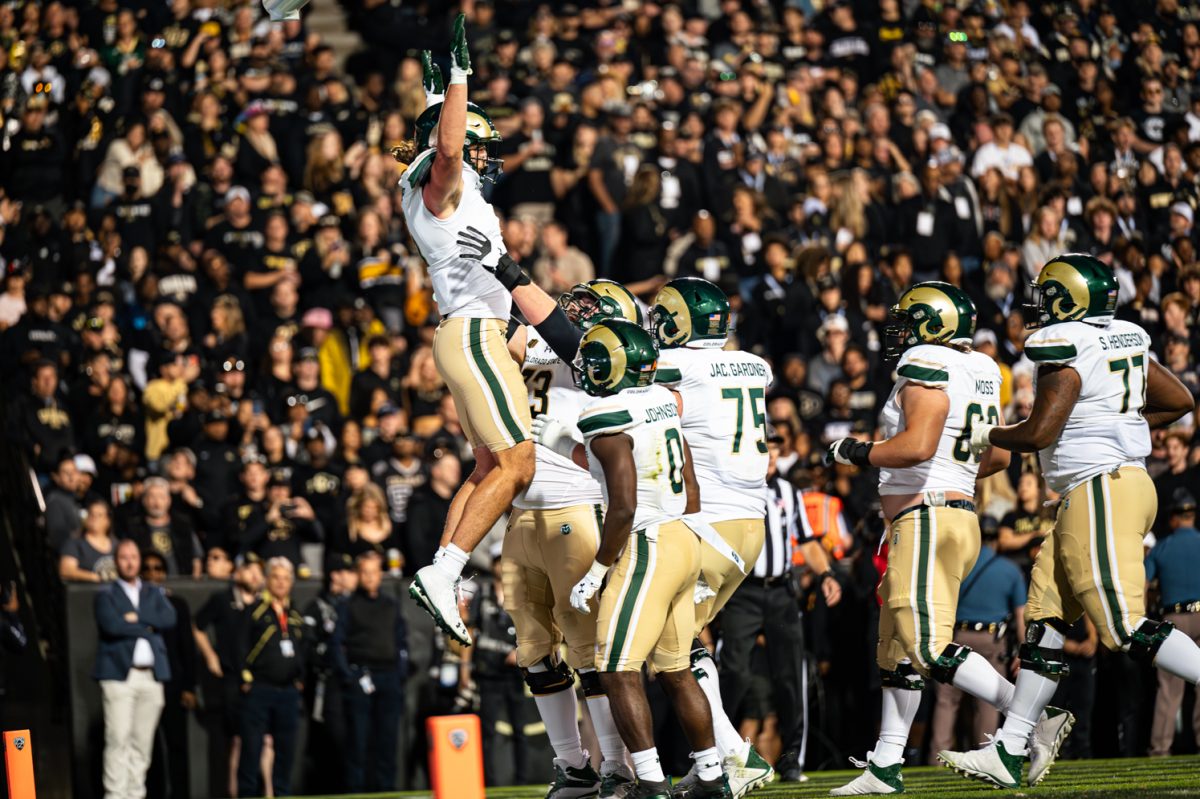 One football player jumps while teammates stand around him. A large crowd of spectators is in the background.