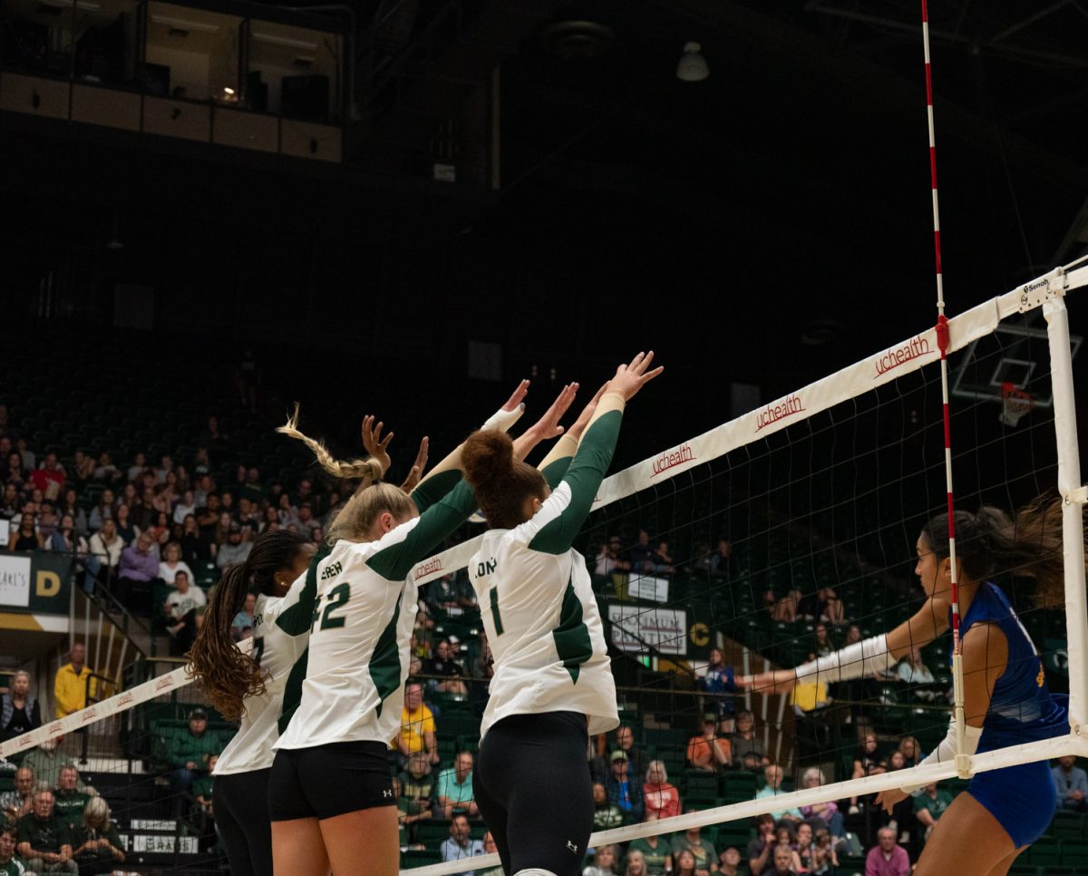 Three Colorado State University volleyball players block a spike from San Jose State.