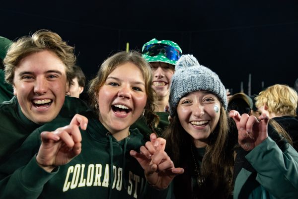 Four young students in green cold weather clothes smile at the camera, one making a ram sign with her hands.