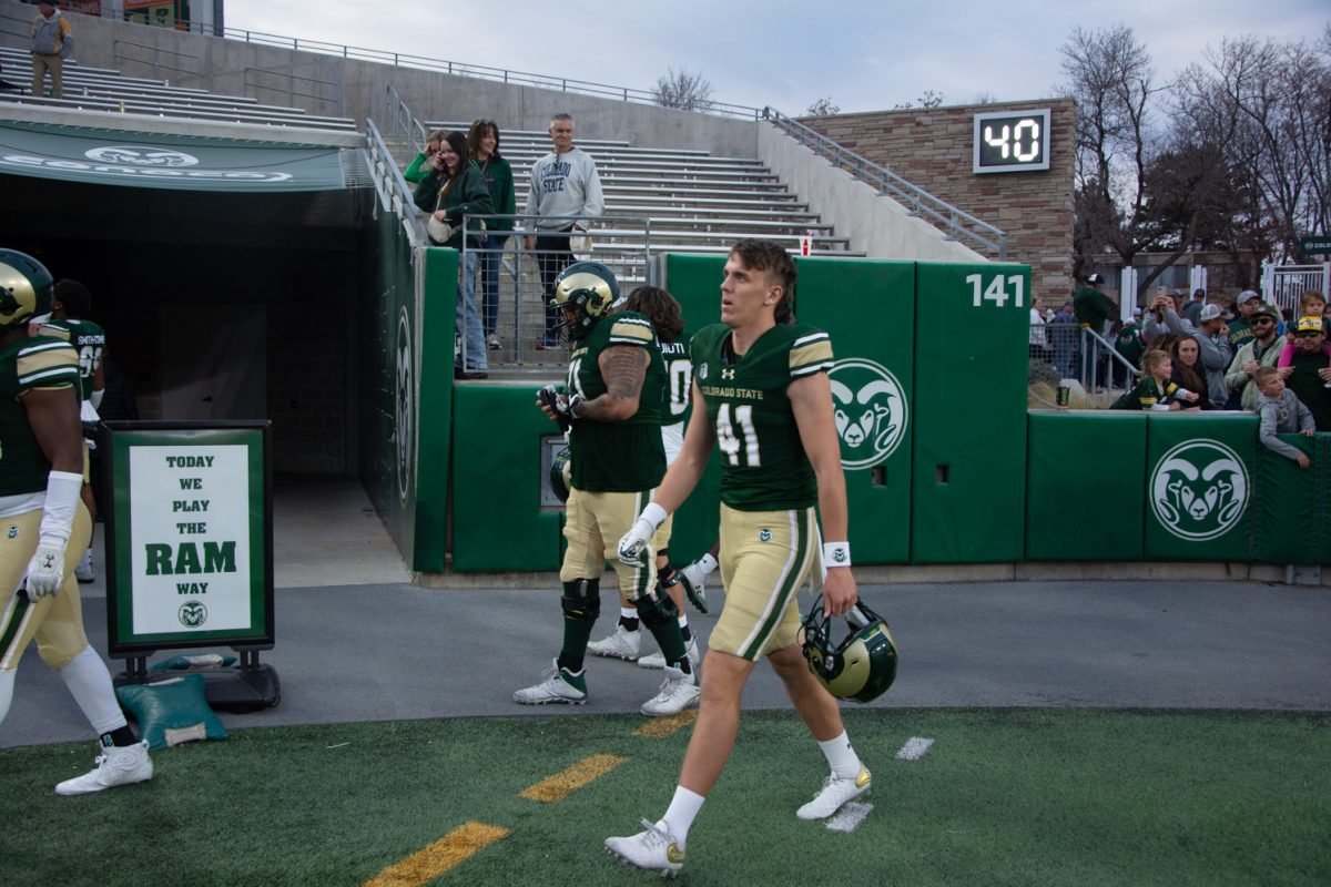 A Colorado State University football player dressed in green and gold walks toward the left side of the field carrying his helmet.