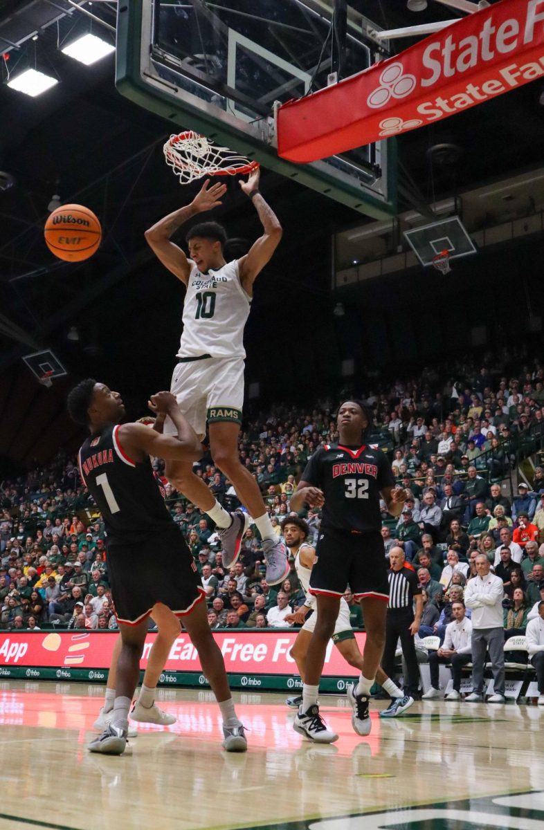 A Colorado State University basketball players wearing a white uniform with green lettering dunks a basketball.