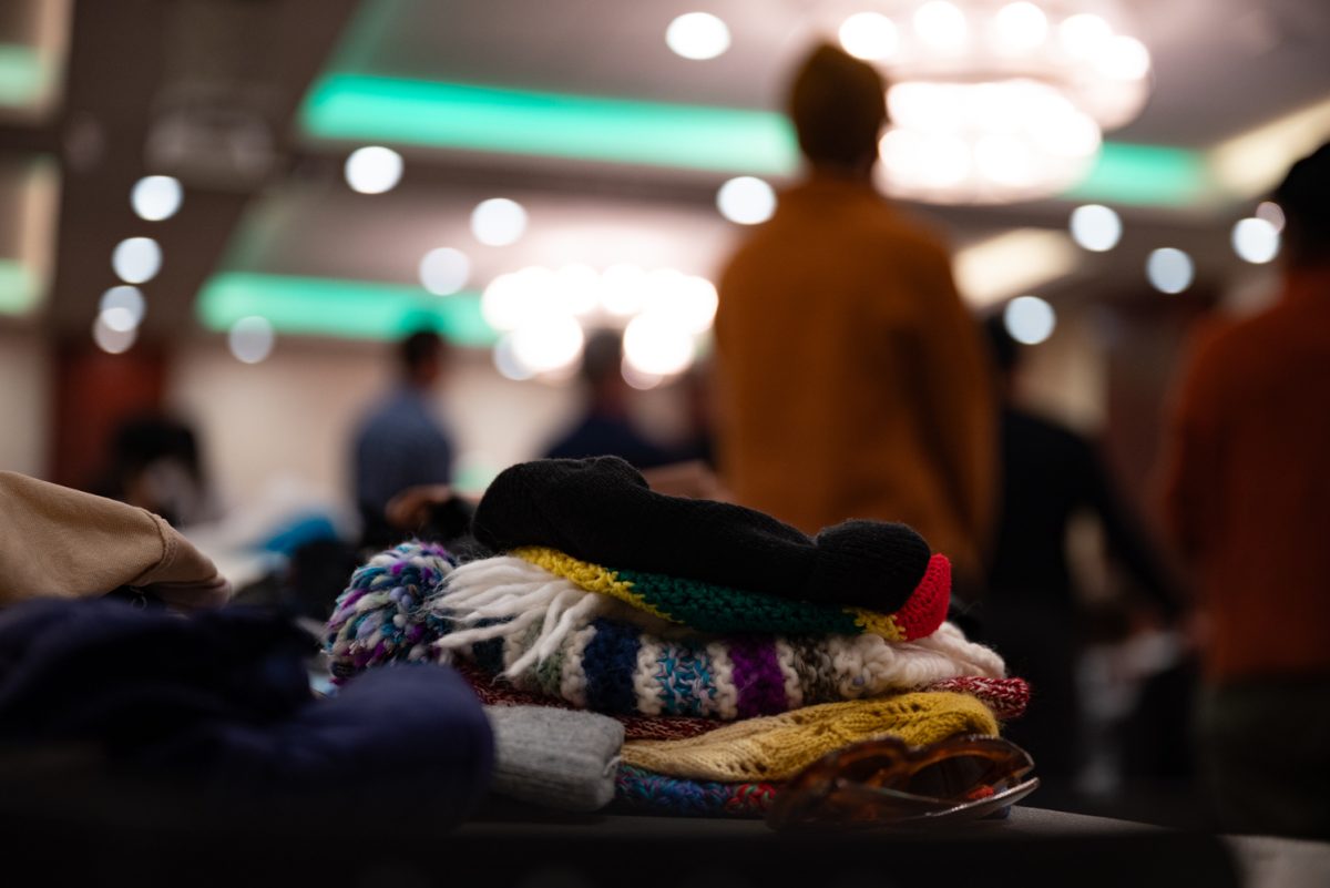 A pile of hats sits on a table while volunteers take a break to listen to a few words from BIPOC Alliance core team member Rashida Perez.