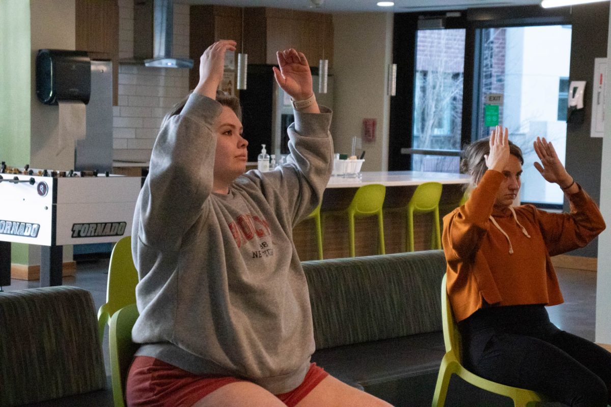 Torin Pruneski and Megan Petersen stretch during seated wheelchair accessible yoga in the Aggie Village Lodgepole lobby on January 29, 2024.