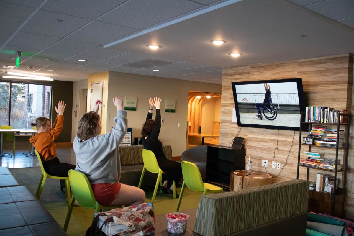 Torin Pruneski, Megan Petersen, and Eve Montoya stretch, following a YouTube video during seated wheelchair accessible yoga in the Aggie Village Lodgepole lobby on January 29, 2024.
