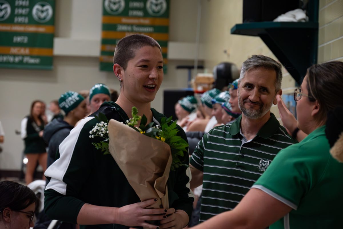 Senior Megan Hager is congratulated by swim coaches Christopher Woodard and Lisa Ginder during senior day celebrations.