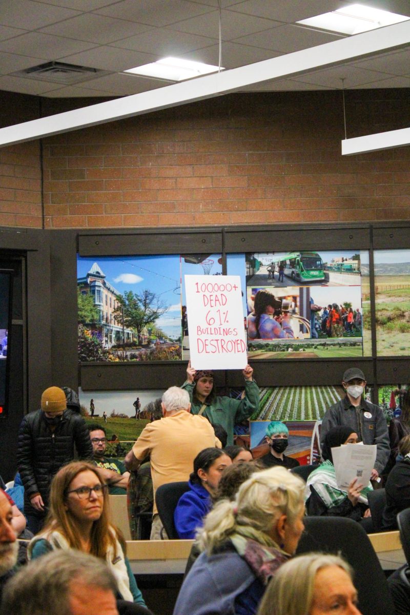 A Fort Collins resident holds up a sign reading !00000+ dead 61% buildings destroyed before the start of the City Council meeting.