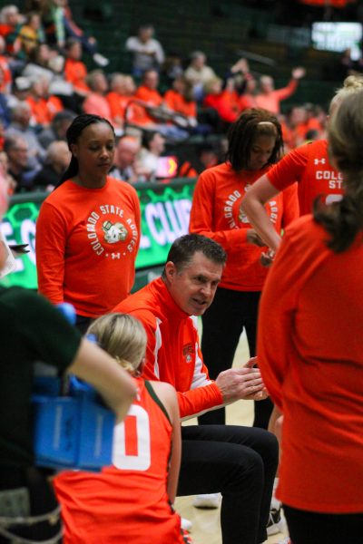 A bunch of women basketball players in orange stand around a man also in orange sitting and talking intently.