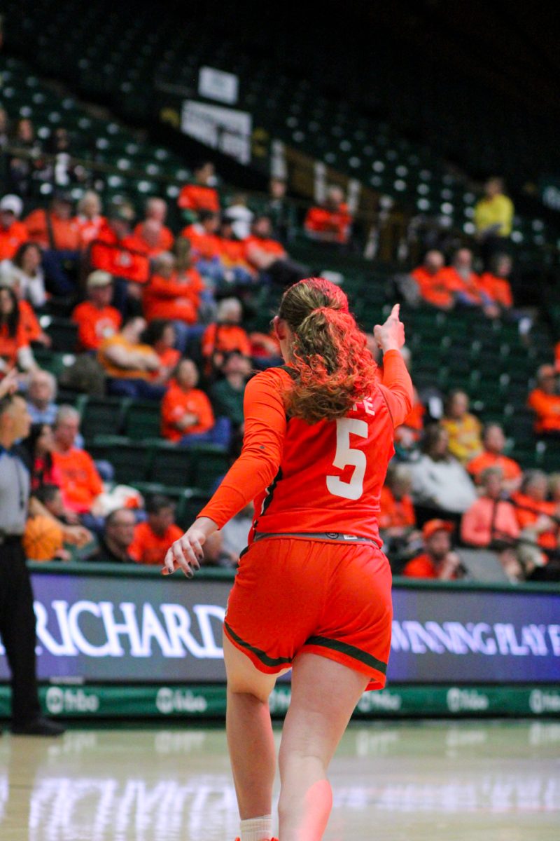 Viewed from behind, a basketball player runs down the court while pointing ahead of her.