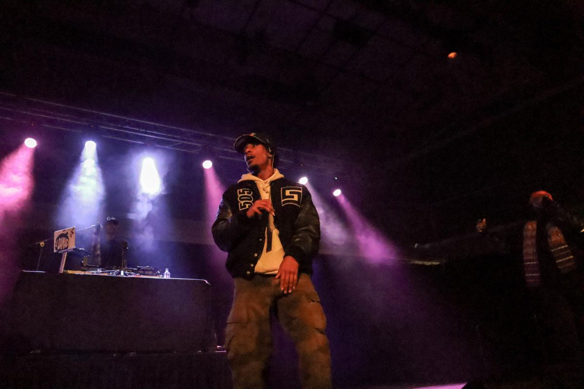 A performer looks up while standing on stage, backed by purple and blue stage lights.
