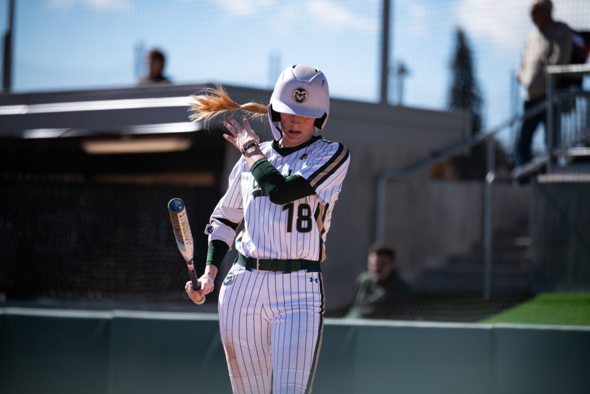 A softball player holding a bat flips her ponytail over her shoulder.