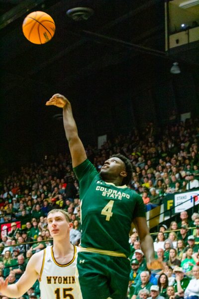 A man in a green uniform shoots a basketball into the air. Another man in white is behind him. Theres a crowd in the stands.