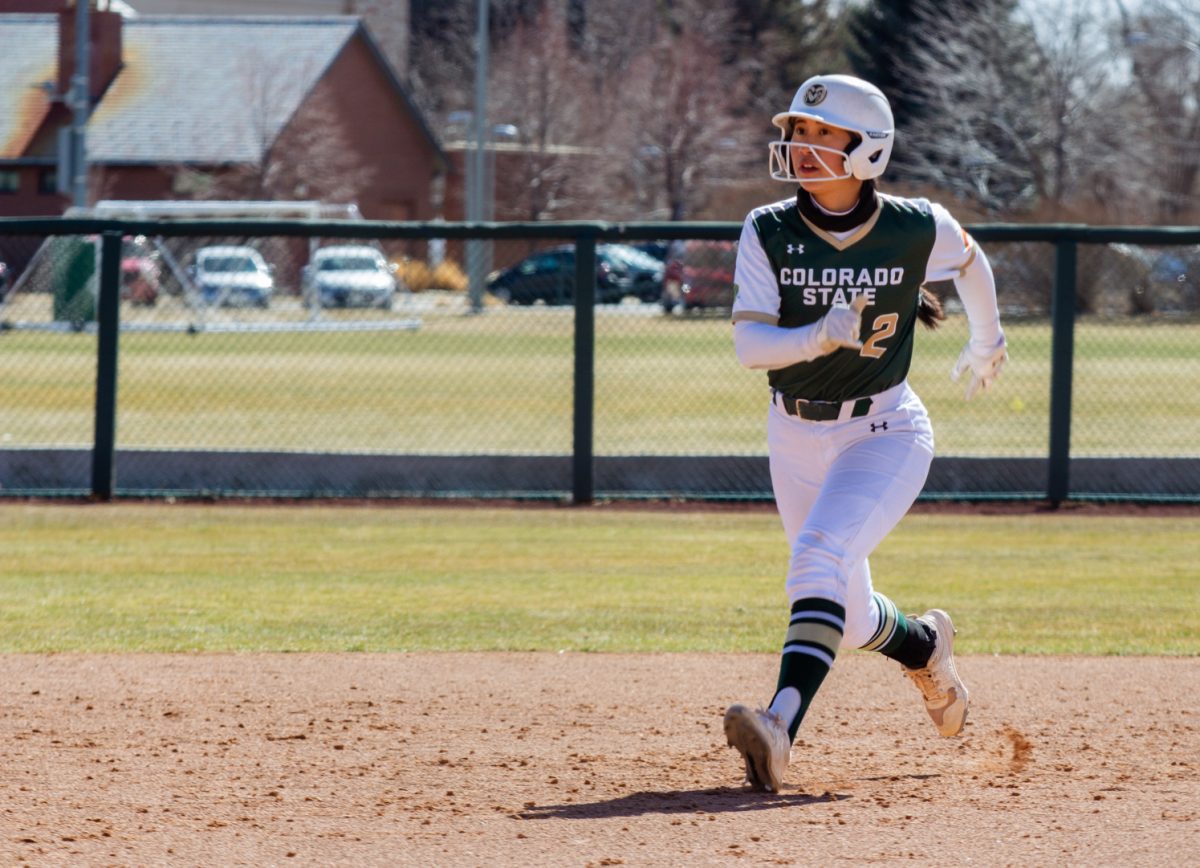 A woman wearing a green and white uniform runs from second to third base while playing softball.