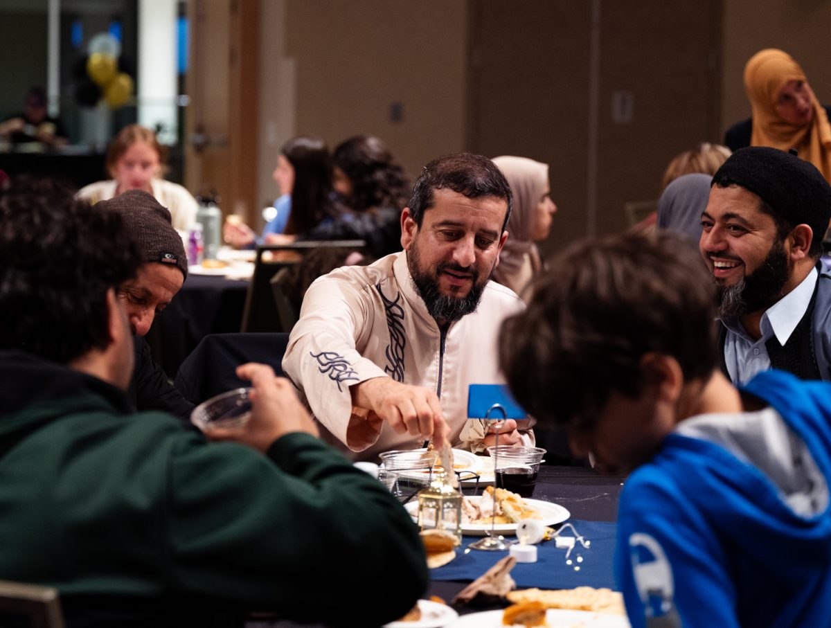 Ahmad Getlawi sits down to eat with friends after leading the call to prayer at the Ramadan Iftar Dinner Event.