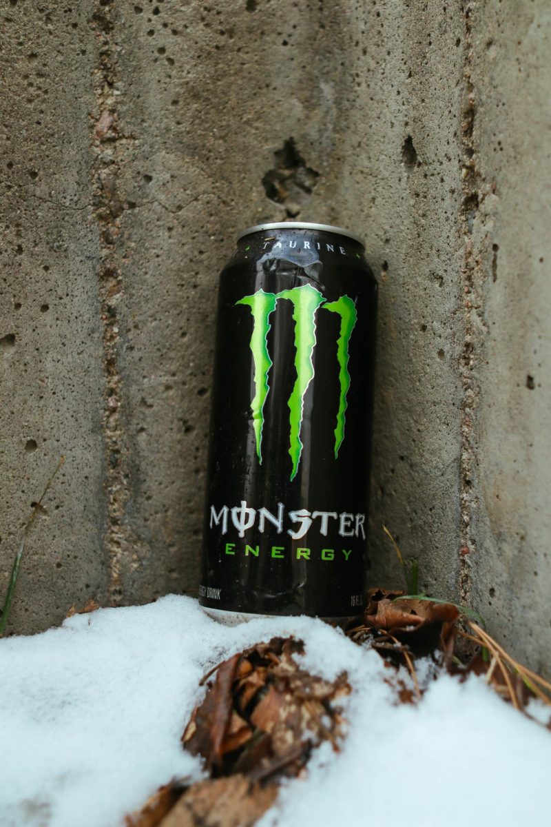 A Coca-Cola Monster Energy drink sits upright in the snow against a concrete wall. March 26.