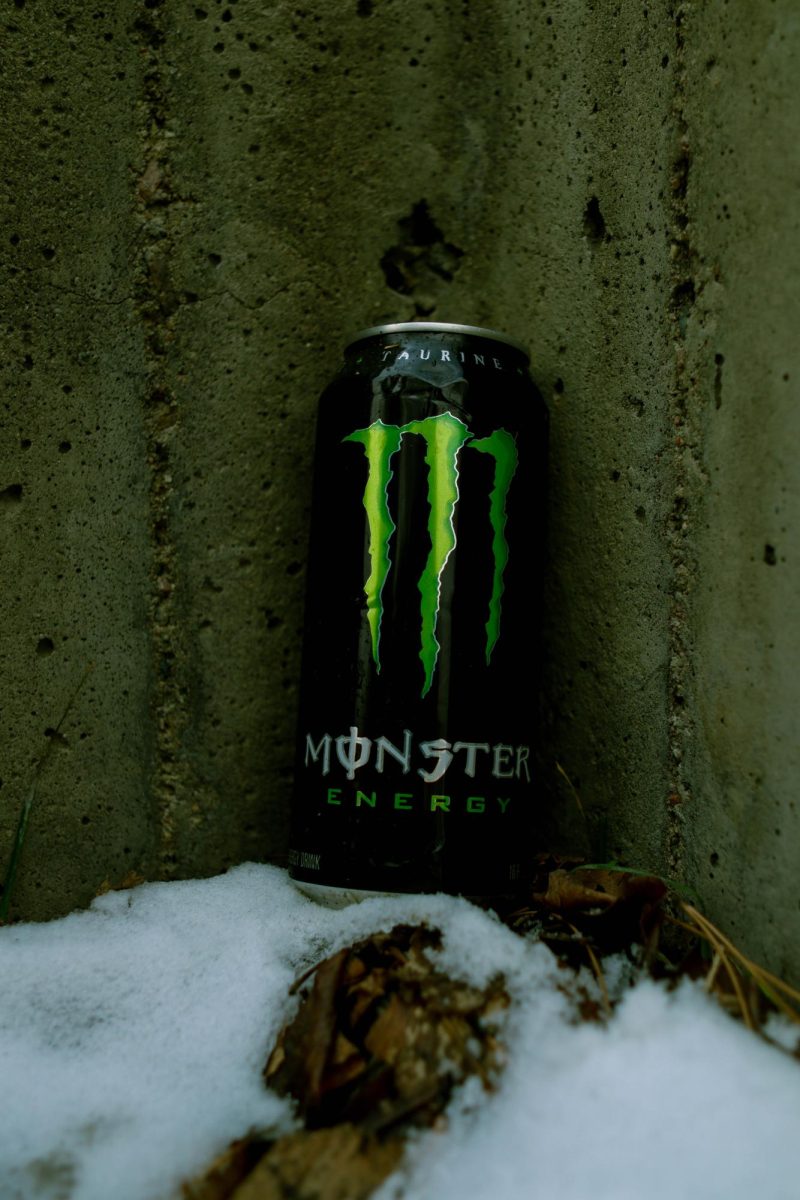 A Coca-Cola Monster Energy drink sits upright in the snow against a concrete wall. March 26.
