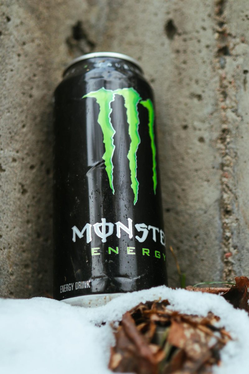 A Coca-Cola Monster Energy drink sits upright in the snow against a concrete wall. March 26.