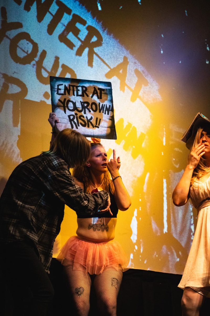 Brad, played by Bekah, and Janet, played by Devour Divinity, read a sign held by Tessa, who also goes by the stage name Yung Ginga, in No Picnics performance of The Rocky Horror Picture Show at The Lyric April 12: Enter at your own risk.