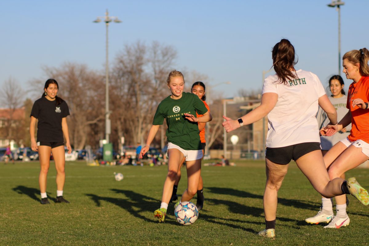A group of women play soccer, the person in the center of the photo smiling and about to kick the ball.