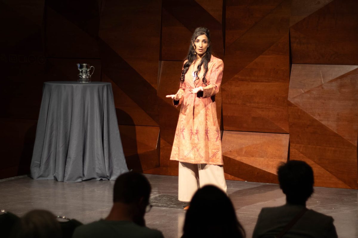 A woman speaks on a stage with her hands held out toward the audience.