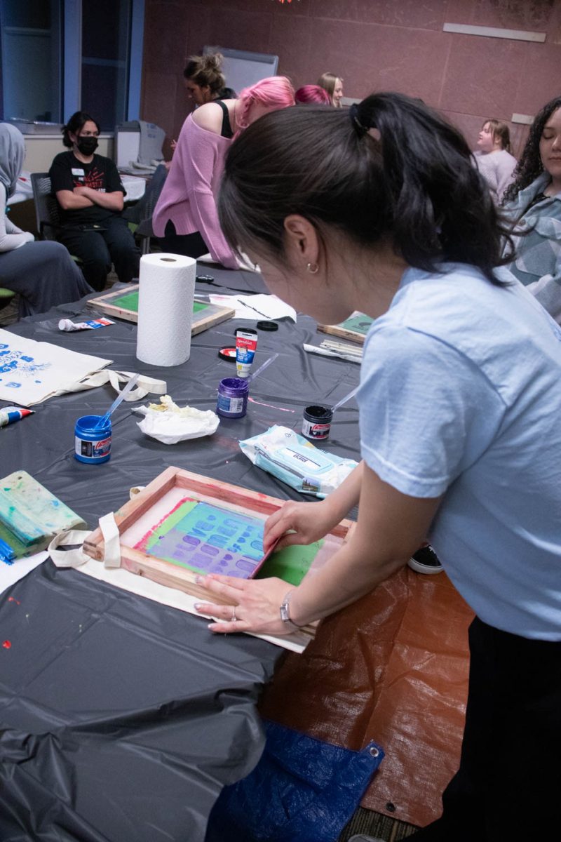 Seojung Lee swipes paint across a silk screen during the Love Women of Color: Celebrating Empowerment Through Art screen printing workshop April 18.