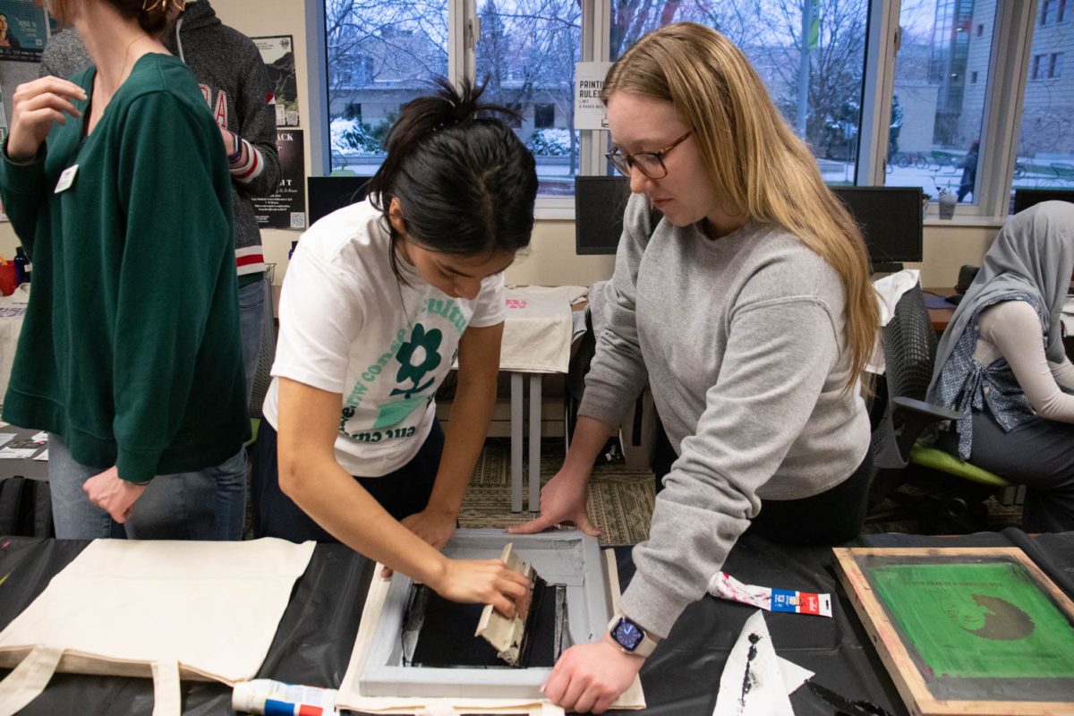 Bianca Escobar prints a design on a tote bag with the help of Rachel Wilcox during the Love Women of Color: Celebrating Empowerment Through Art screen printing workshop April 18.