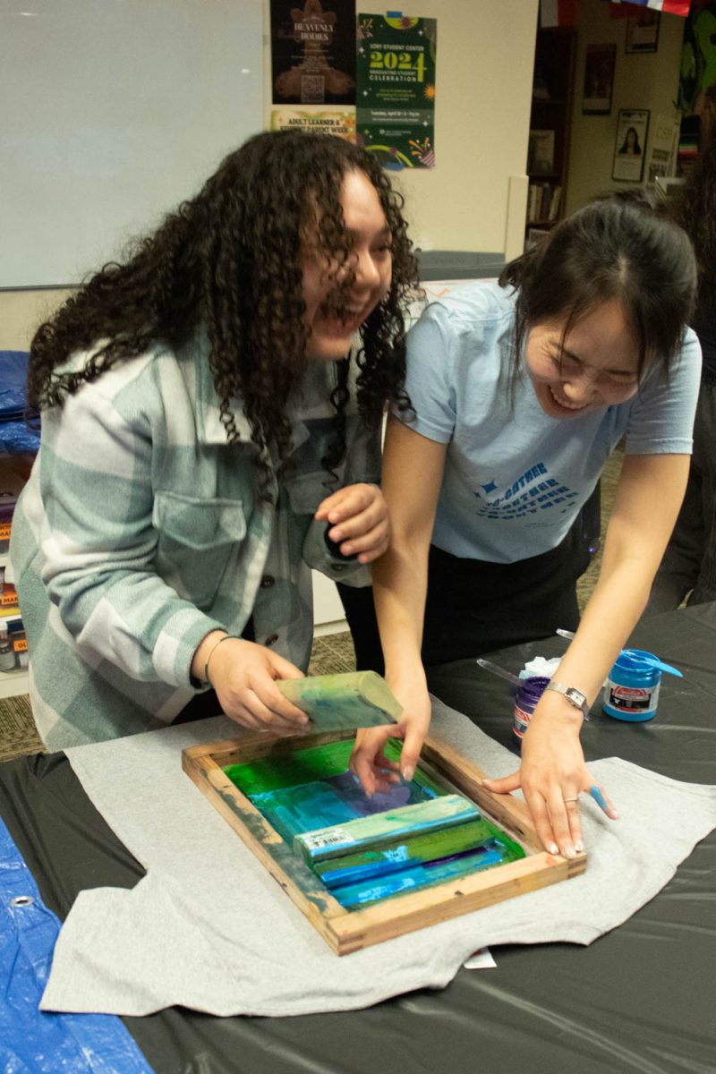 Angelita Chavez and Seojung Lee laugh after the scraper broke while working on screen printing on a t-shirt during the Love Women of Color: Celebrating Empowerment Through Art screen printing workshop April 18.