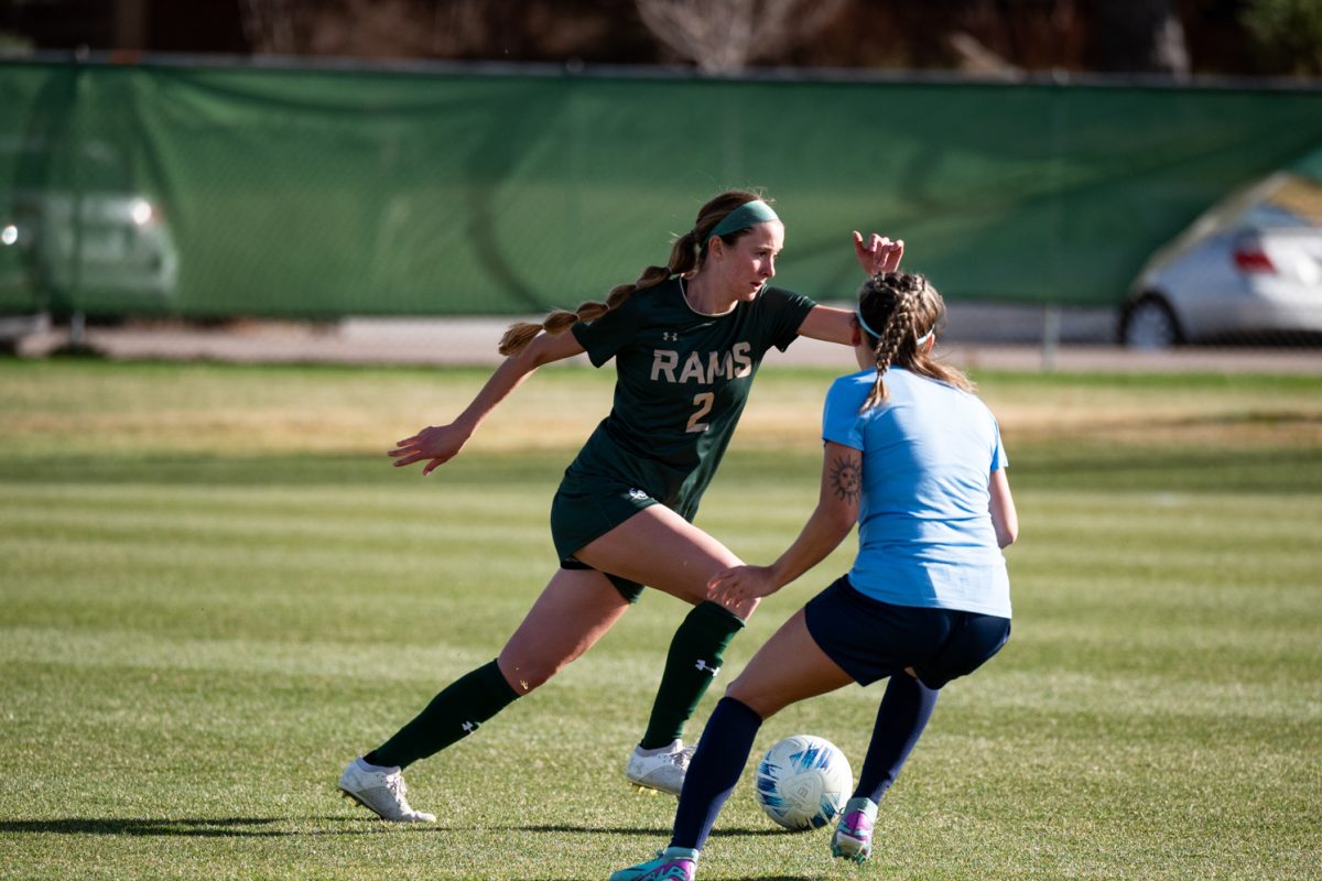 One soccer player dribbles across the field while another tries to steal the ball.