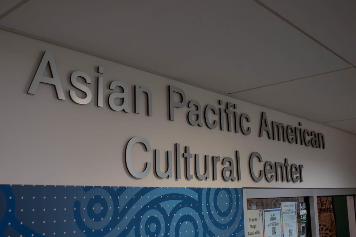 The words Asian Pacific American Cultural Center in silver lettering are attached to the wall above the entrance to a room.