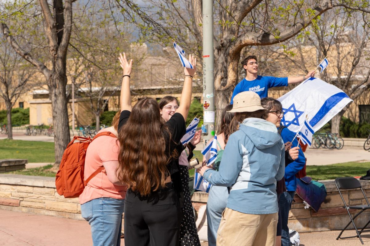 Viewed from behind, several students stand in a group, each holding an Israel flag.