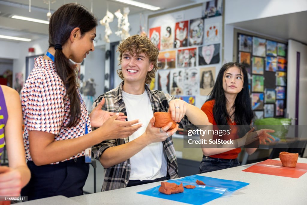 Group of students participating in an art class while at school in the North East of England. They are using modelling clay and a teacher is helping them through the process.