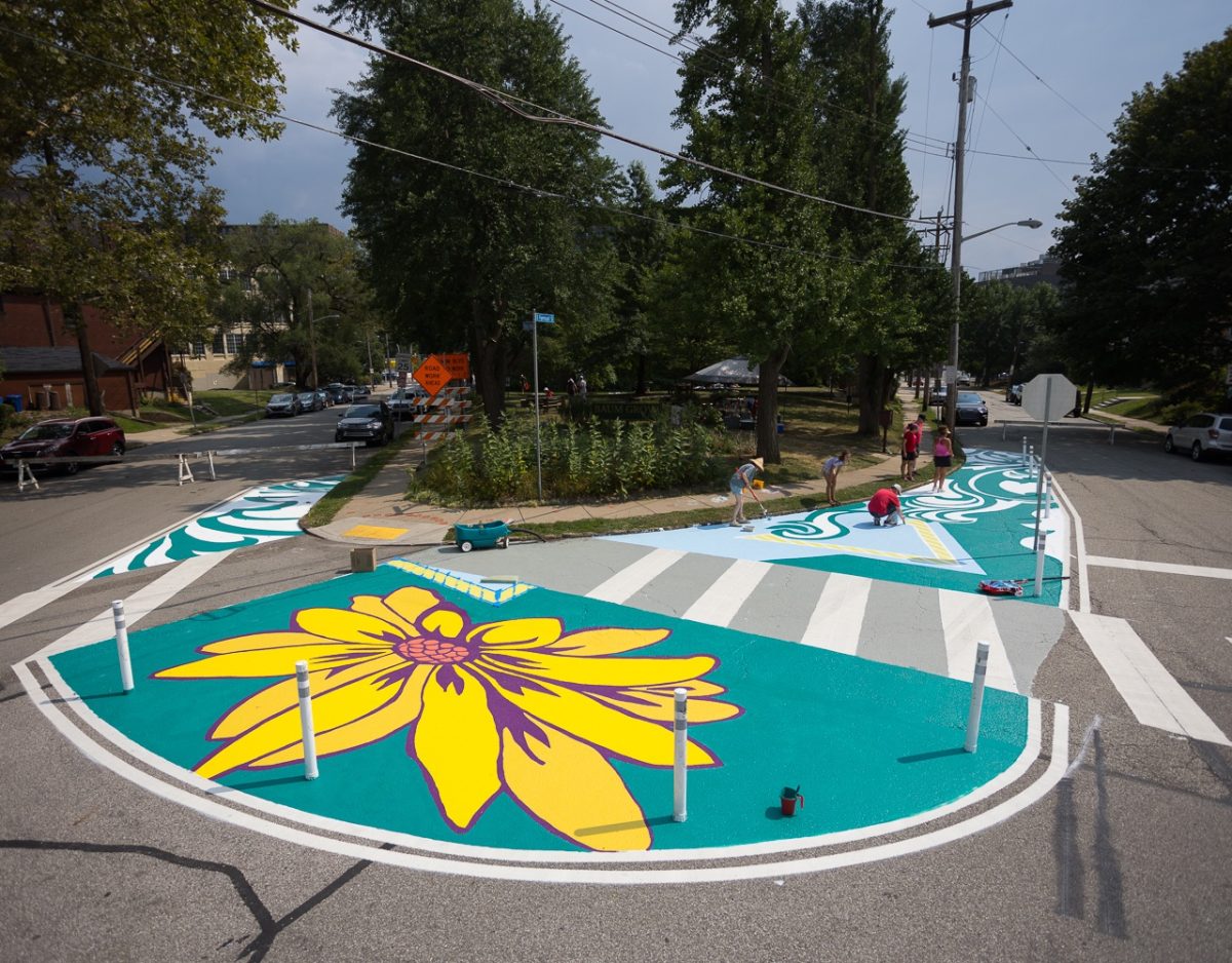 A road island with protruding crosswalks surrounded by yellow flowers on a teal background painted on the asphalt.