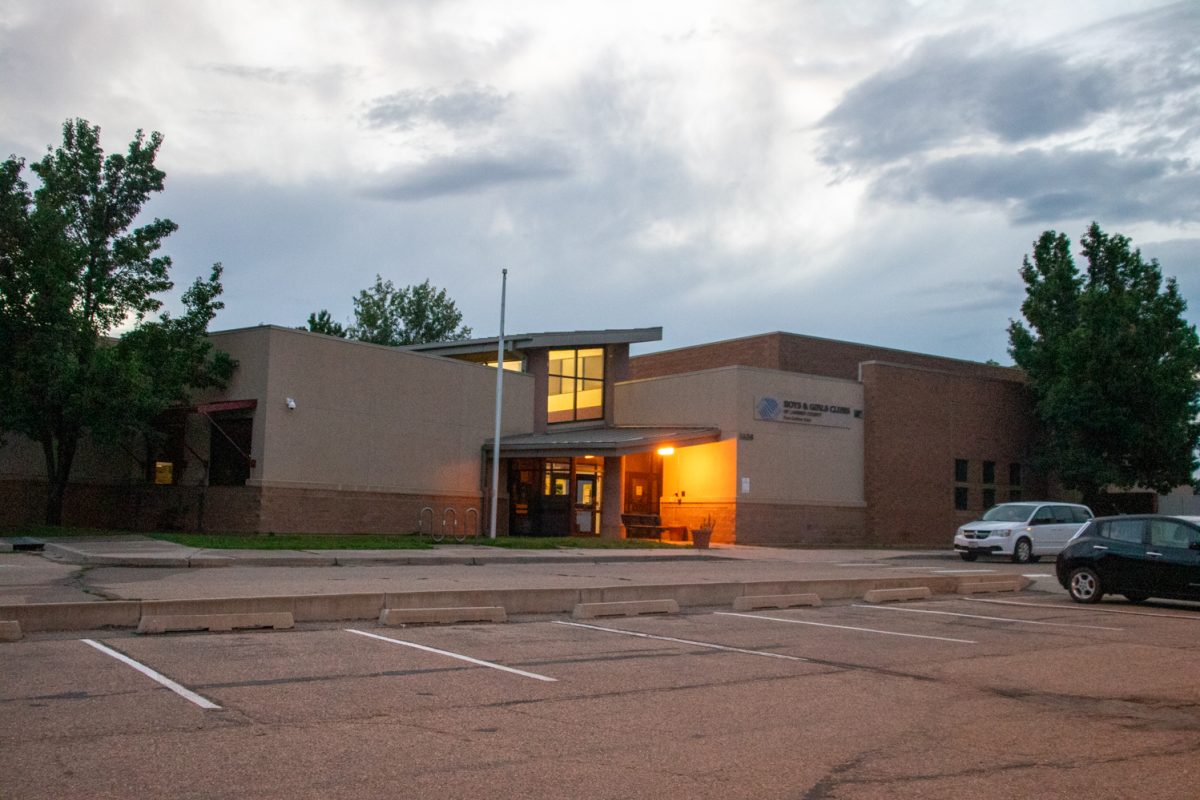 The exterior and parking lot of a building with a white car parked on the right. A sign on the building says "Boys and Girls Club of Larmier County Fort Collins Club.