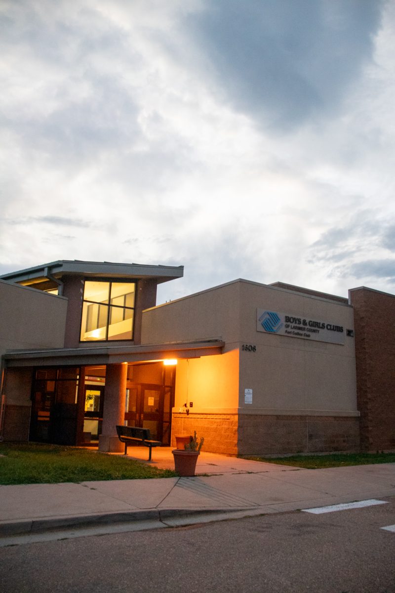 The exterior and parking lot of a building with a white car parked on the right. A sign on the building says "Boys and Girls Club of Larmier County Fort Collins Club.