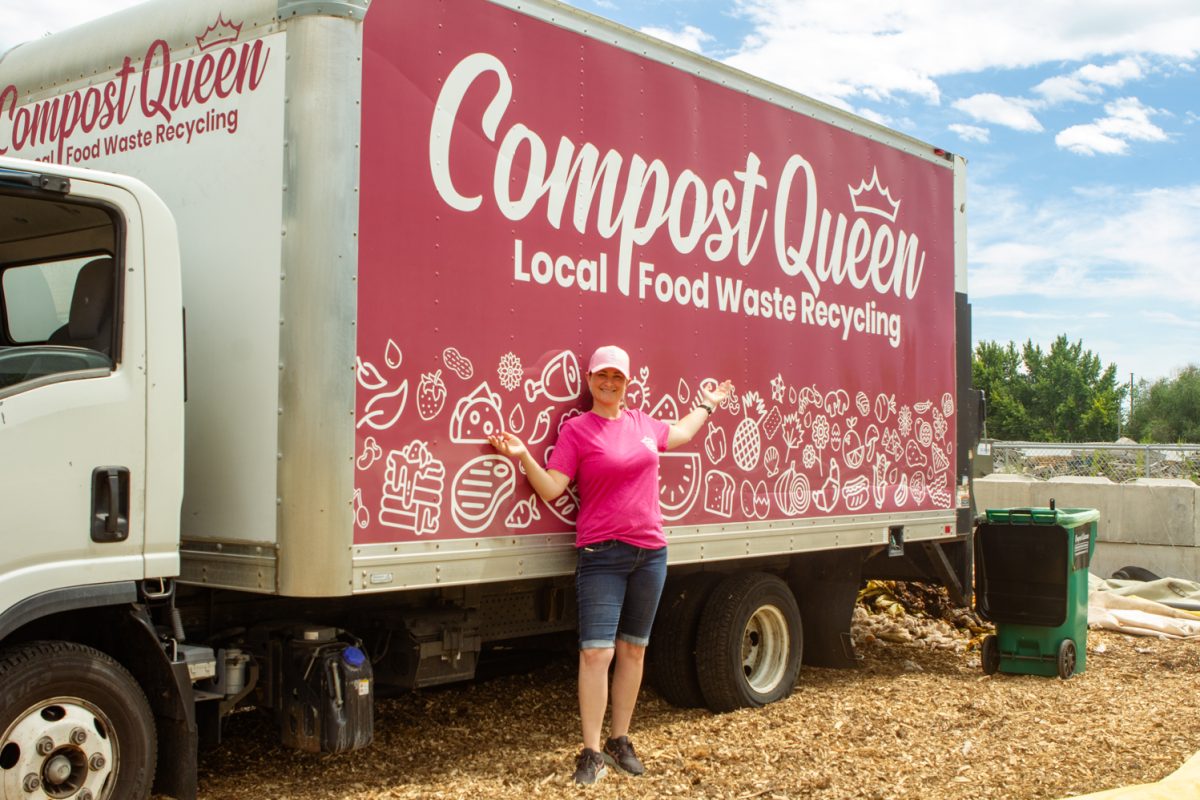 A woman wearing a hot pink shirt and light pink hat stands next to a large red-pink delivery truck that reads "Compost Queen Local Food Waste Recycling."