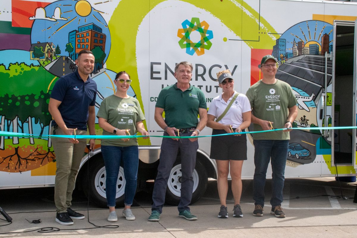 Five people stand smiling preparing to cut a green ribbon in front of a bus like vehicle with Energy Institute written on the side.