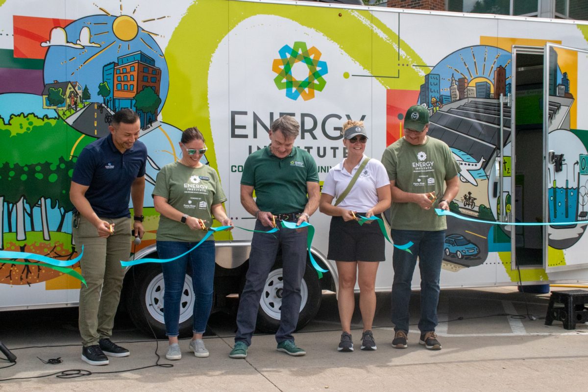Five people are cutting a ribbon in front of a trailer with colorful energy-related designs on it.