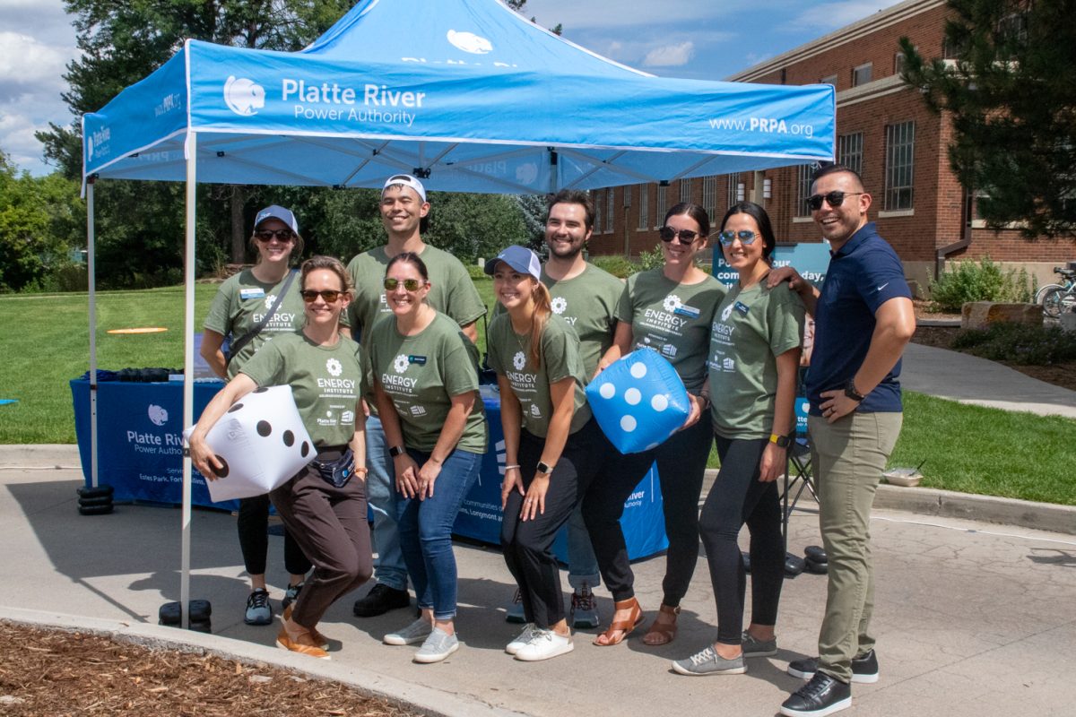Nine people smile and pose for a picture in front of a tent and tables outside.