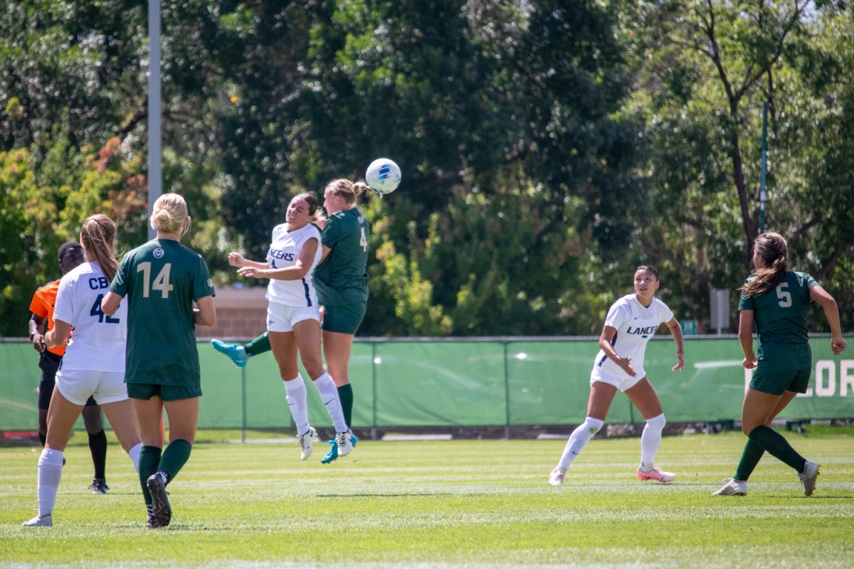 2 soccer players from opposing teams jump into the air.