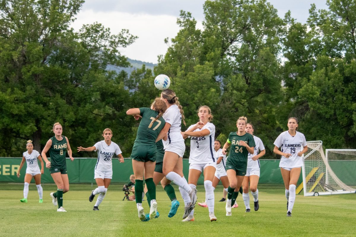 2 soccer players jump for the ball while others run toward them.