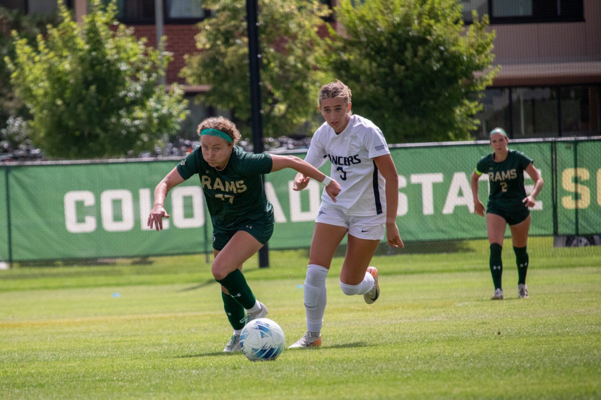 Two soccer players, one from each team run to try to get the ball.