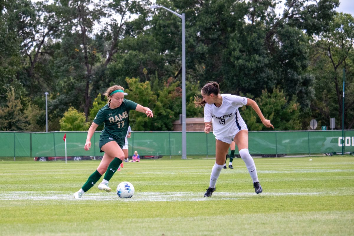 A soccer player in a green jersey kicks the ball while a player in a white jersey defends her.
