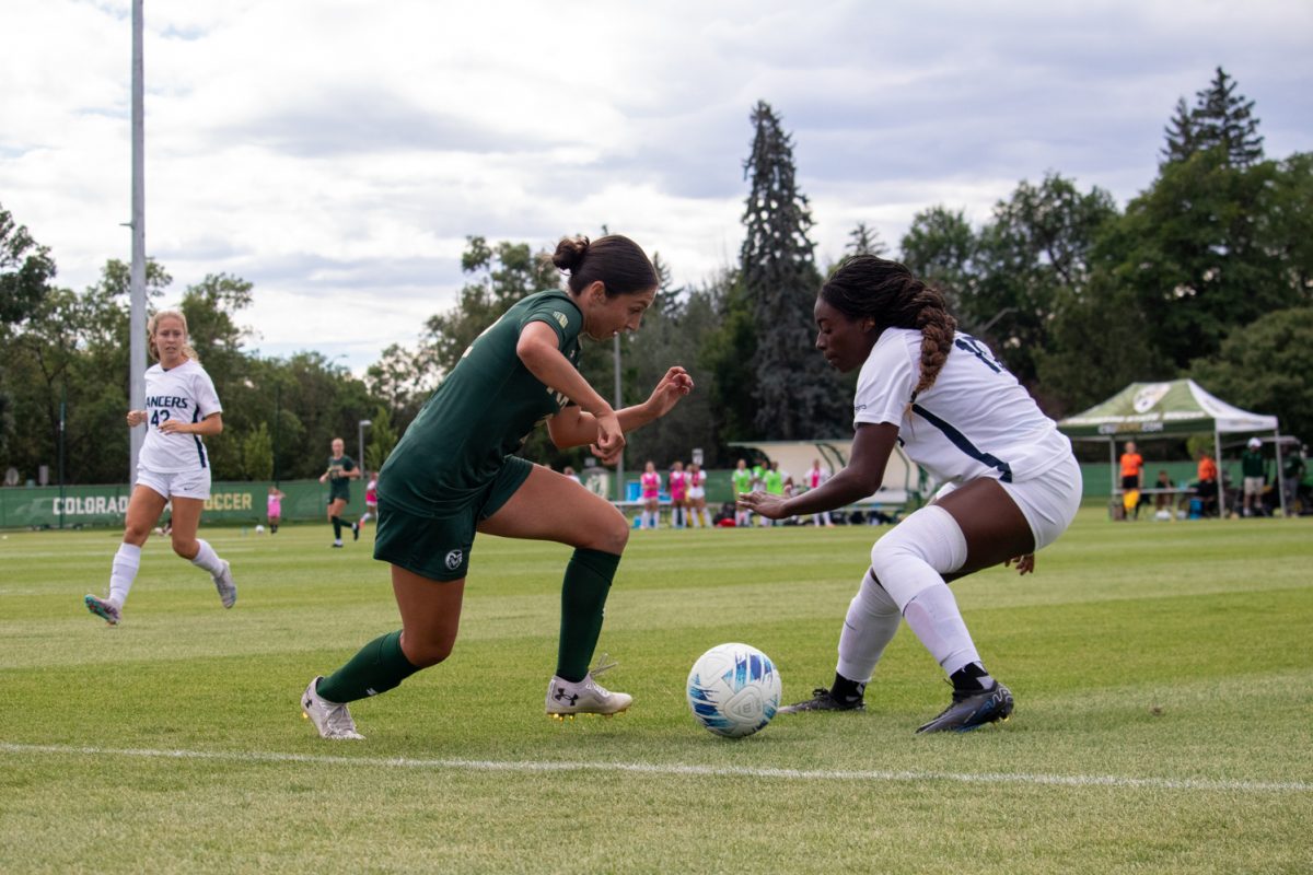 A soccer player tries to kick the ball while another player from the other team defends her.