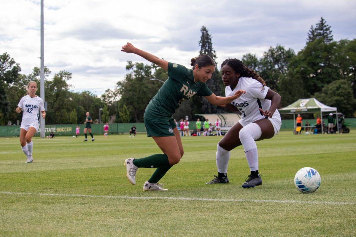 A soccer player tries to kick the ball while another player from the other team defends her.