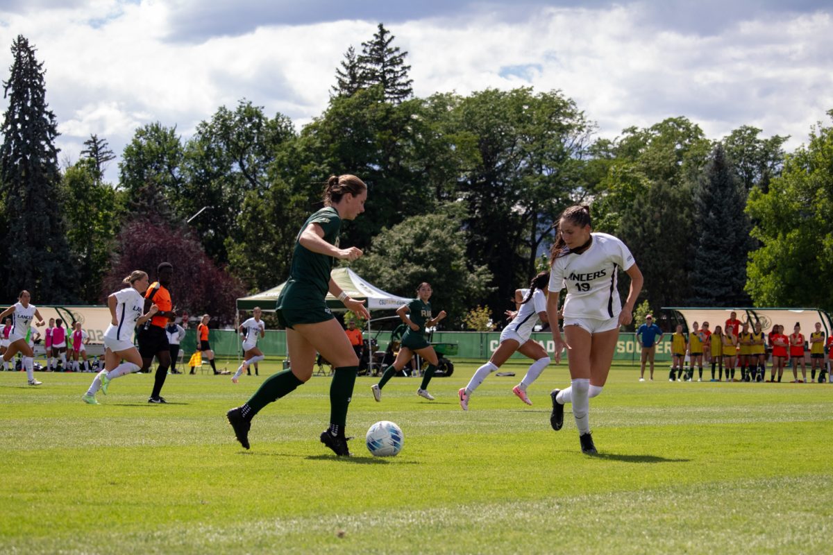 A soccer player kicks the ball while a player from the opposing team tries to stop her.