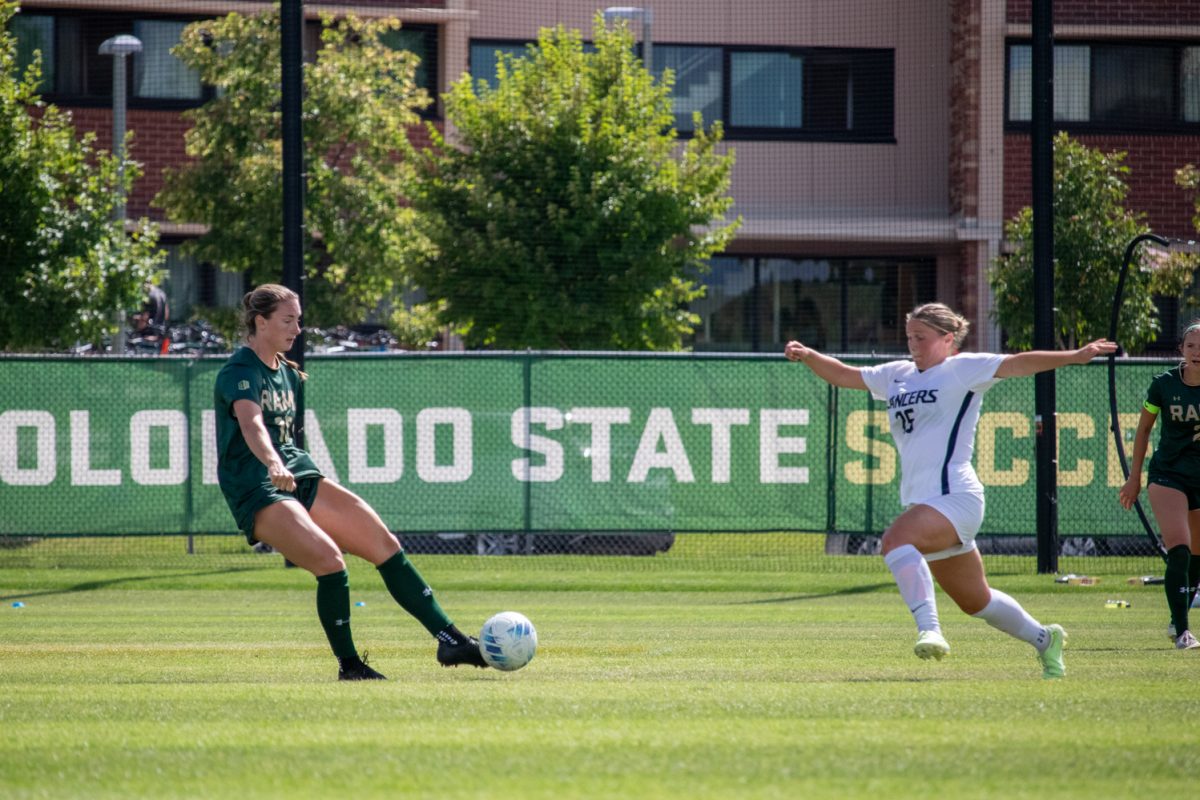 A soccer player kicks the ball while a player from the other team stretches to try to block it.