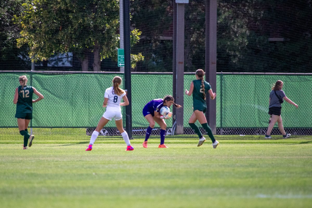 A soccer goaltender bends down to grab the ball.